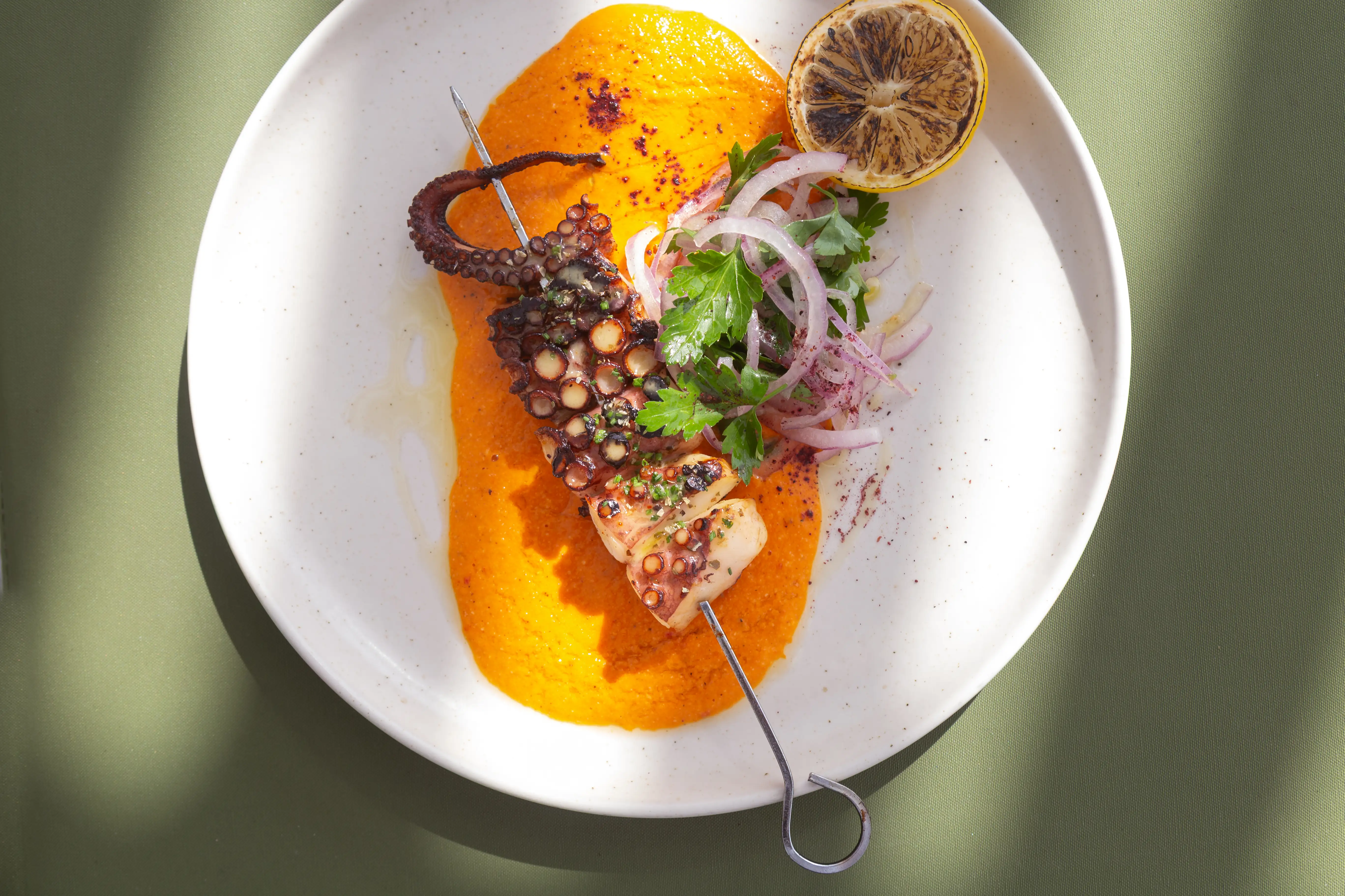 Octopus souvlaki plated with roasted pepper puree and onion salad